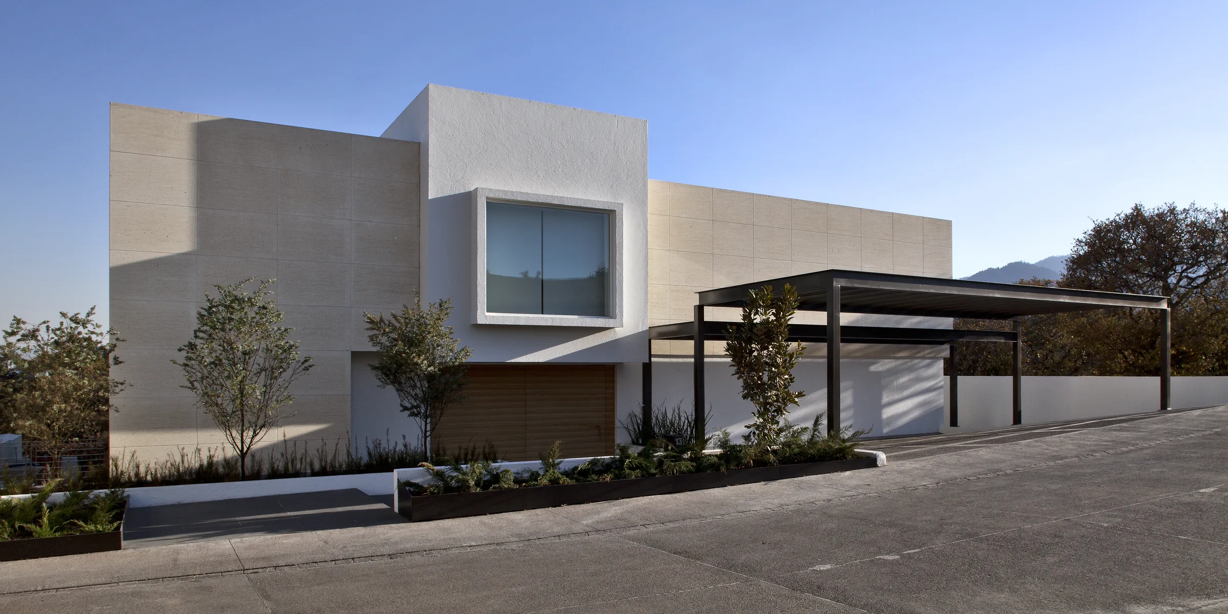 Residencia contemporánea de piedra caliza y estuco blanco, con cochera, bajo un cielo despejado y montañas al fondo.
