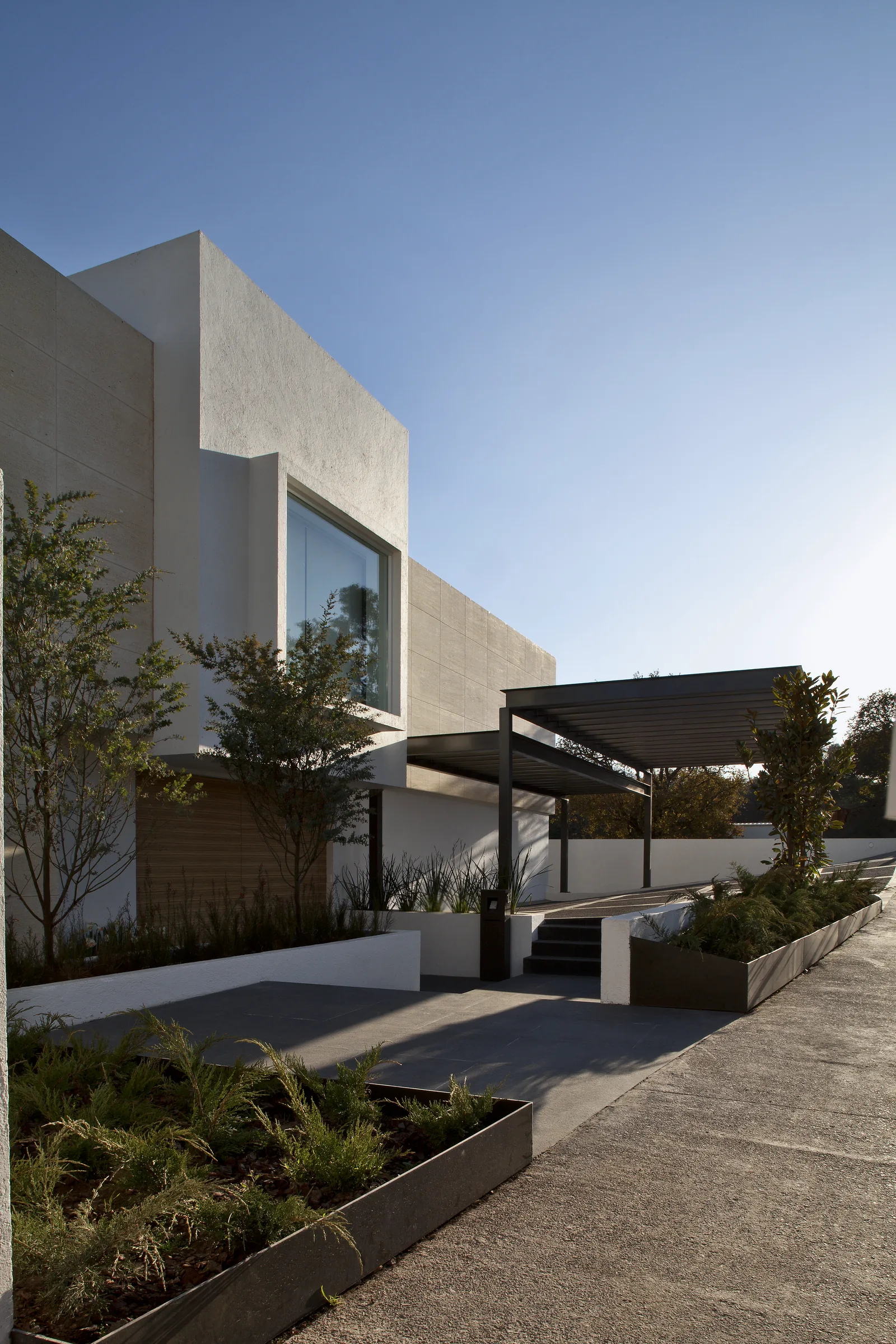 Acceso lateral de la residencia, con la pérgola de acero y la jardinería.